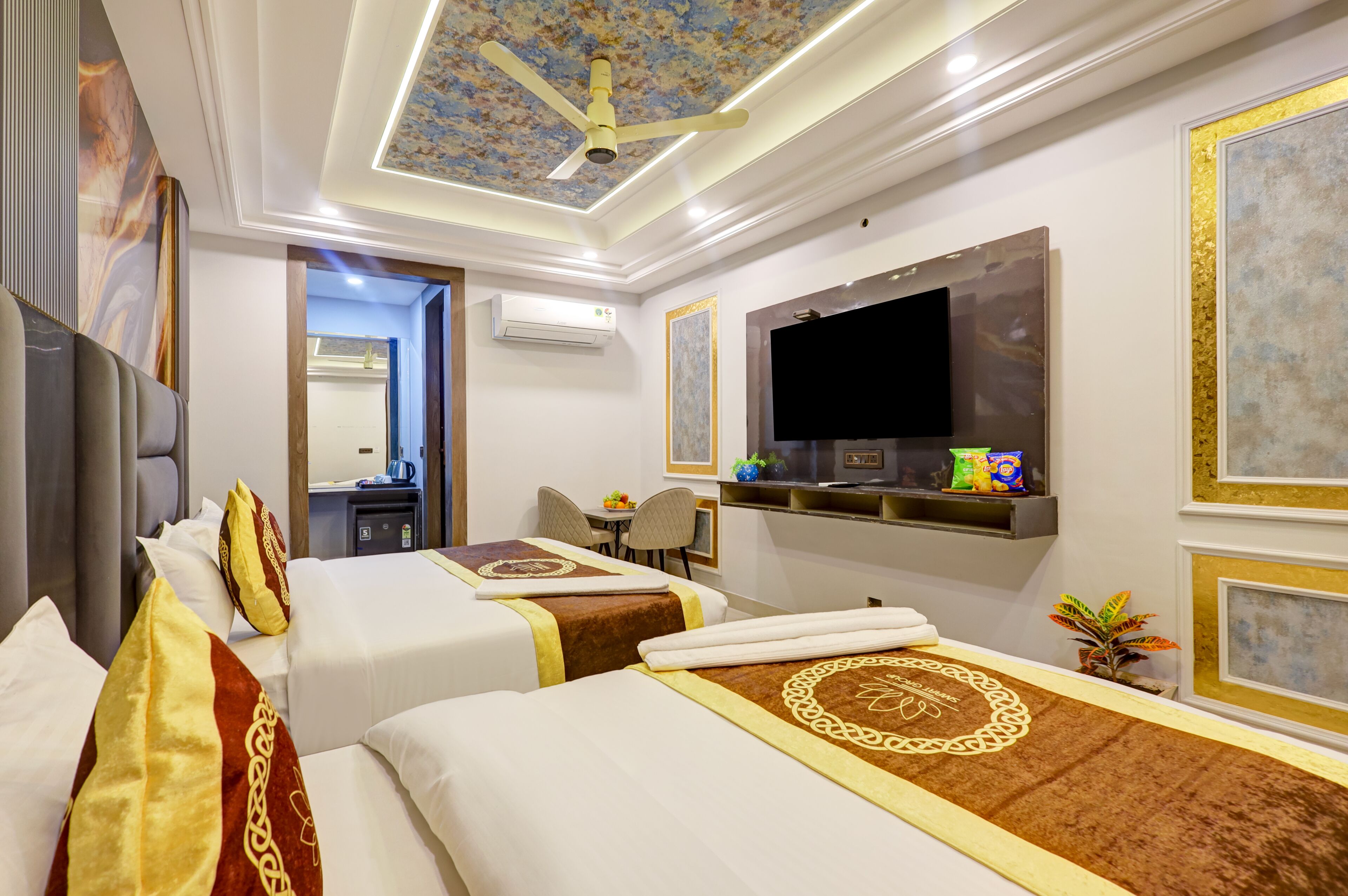 A hotel room with two beds, a ceiling fan, a flat-screen TV, a small desk, and a seating area.