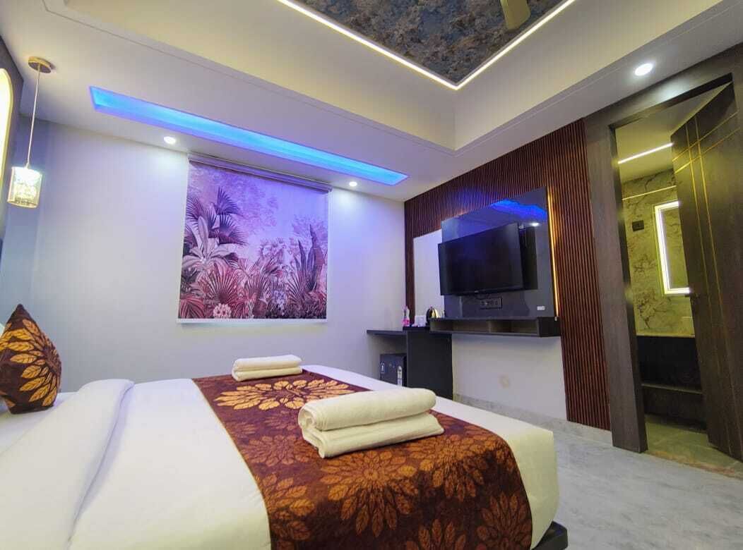 A modern hotel room with a large bed, a flat-screen TV, and a ceiling with blue LED lighting.