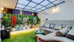 A modern interior with a glass ceiling, a sofa set, potted plants, and a small table with bottles.