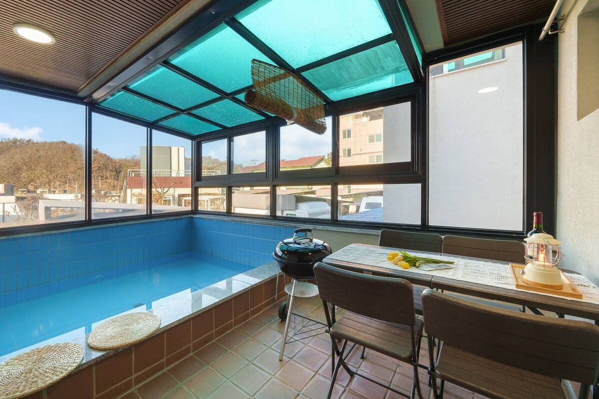A sunlit indoor pool area with a view of buildings and hills.