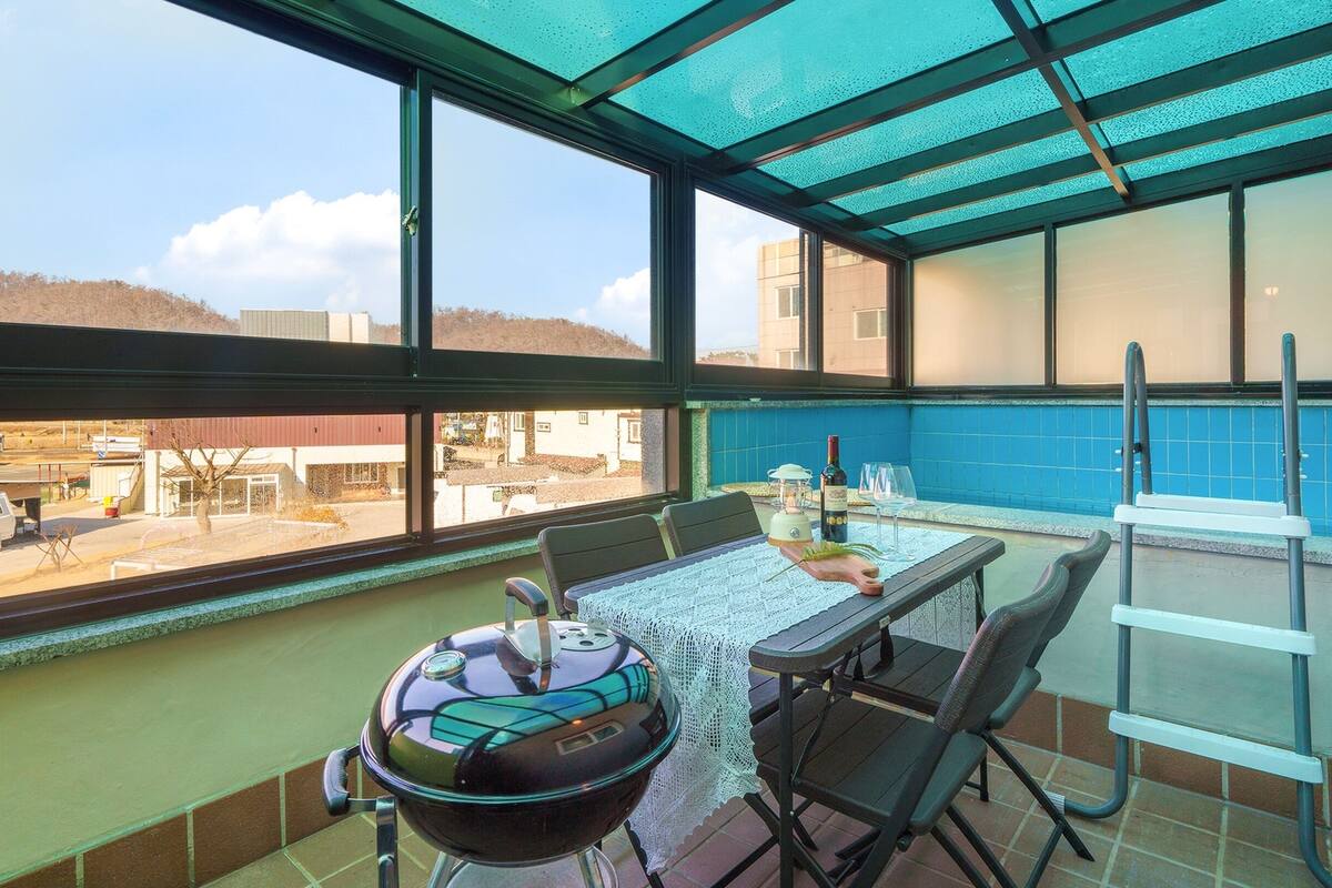 A balcony with a table, chairs, a grill, and a view of the parking lot.