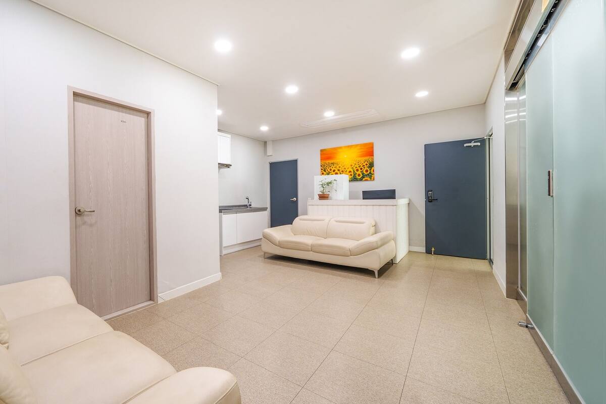 A modern living room with a beige sofa, a small kitchen area, and a dining table.