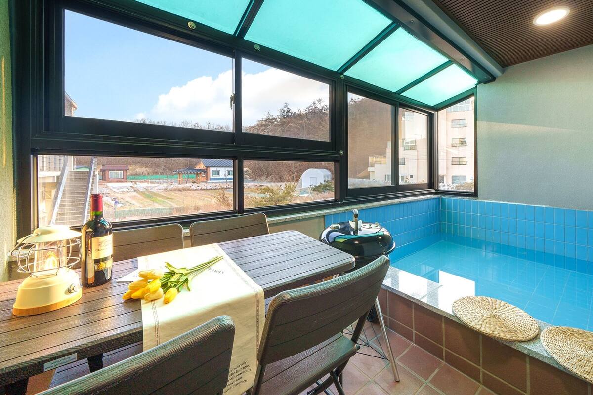 A poolside area with a table, chairs, and a bottle of wine.