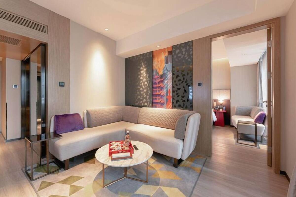 A modern hotel room with a sectional sofa, a round coffee table, and a cityscape mural on the wall.