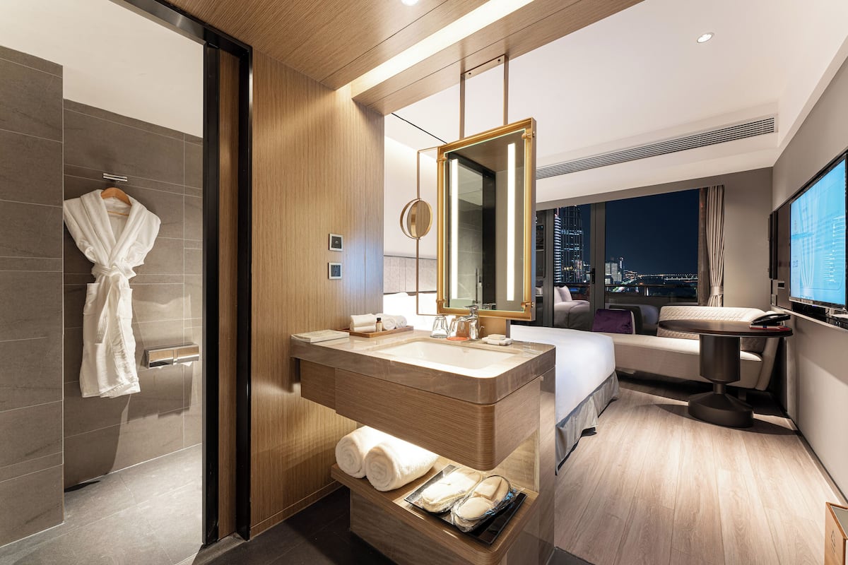 A modern hotel bathroom with a large mirror, a sink, and a shower area.