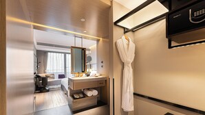 A modern hotel room with a wooden floor, a large mirror, a vanity with a sink, and a robe hanging on a rack. - Ethos Hotel Wuhan Riverside (Wuhan)