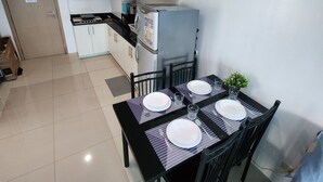 A compact kitchen with white cabinets, a refrigerator, and a dining table set for four with plates and cutlery. - Spacious 2BR at Sea Residences Near MOA - Family Stay (Pasay)