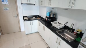 A kitchen with white cabinets, a black countertop, a sink, and a stove. - Spacious 2BR at Sea Residences Near MOA - Family Stay (Pasay)