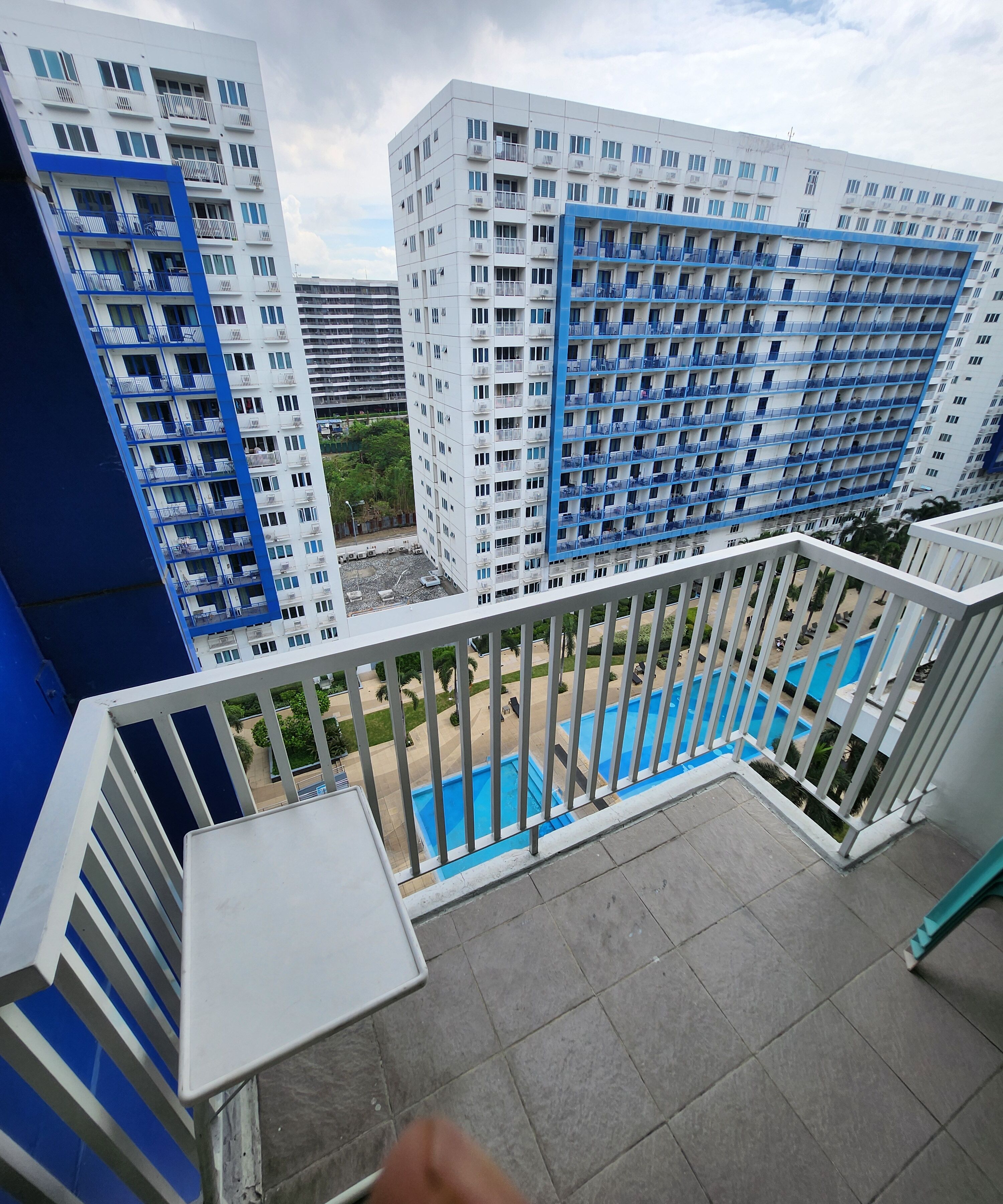 A high-rise residential building with multiple balconies, a swimming pool, and a view of surrounding buildings.
