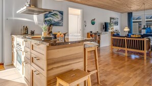A modern kitchen with a wooden island, bar stools, and a dining area with a blue sofa. - "Kaapo" - 300m from the sea by Interhome (Løkken)