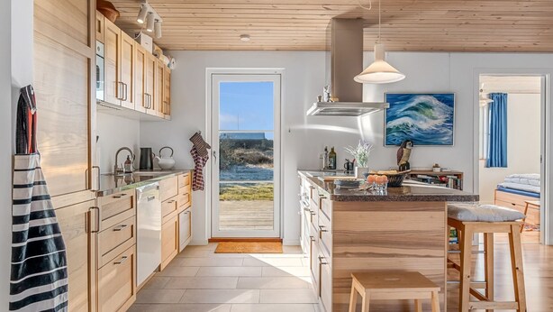 A modern kitchen with wooden cabinets, a large island, and a view of the outdoors. - "Kaapo" - 300m from the sea by Interhome (Løkken)