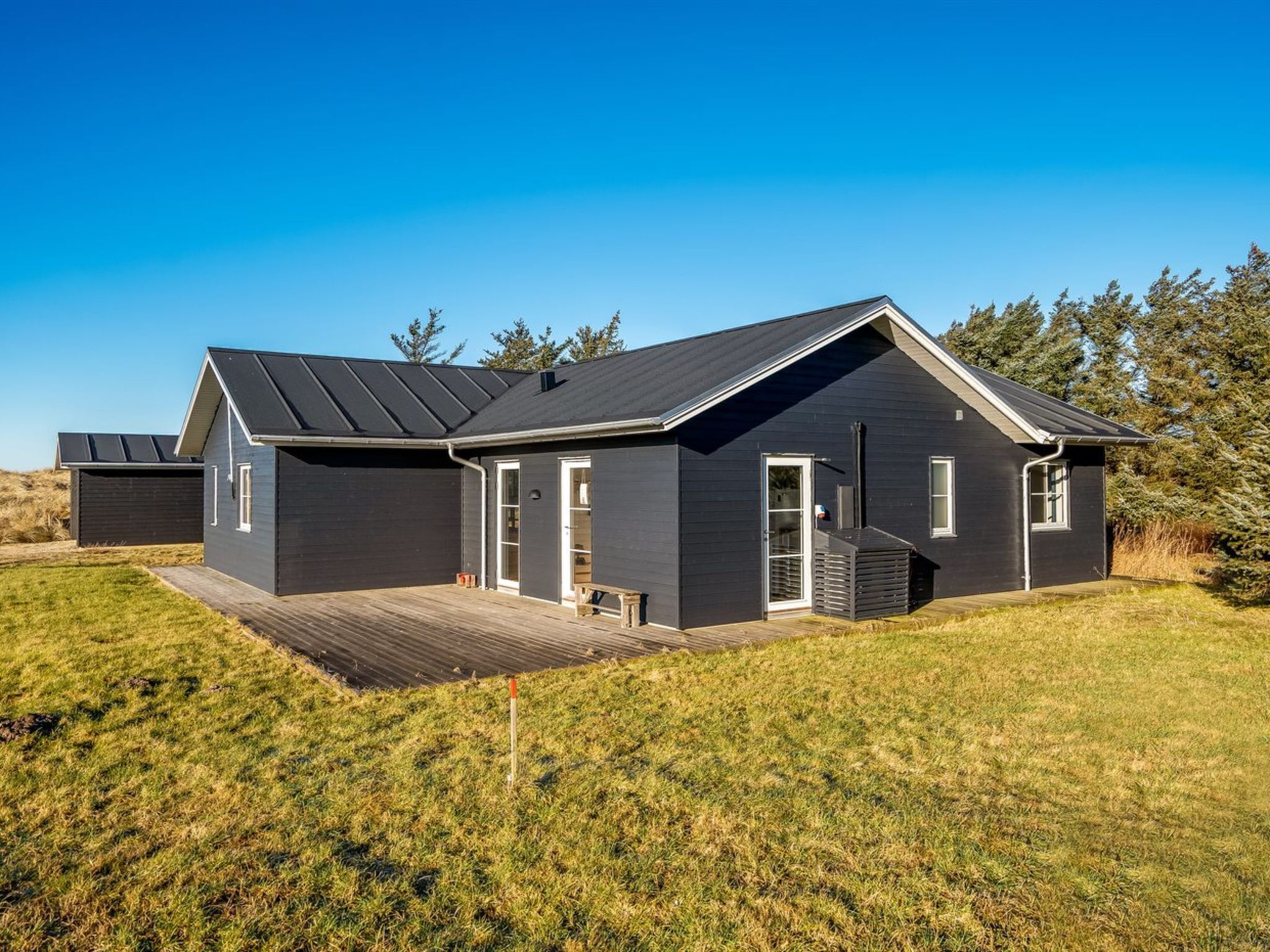 A modern two-story house with a dark exterior, a sloped roof, and a wooden deck.