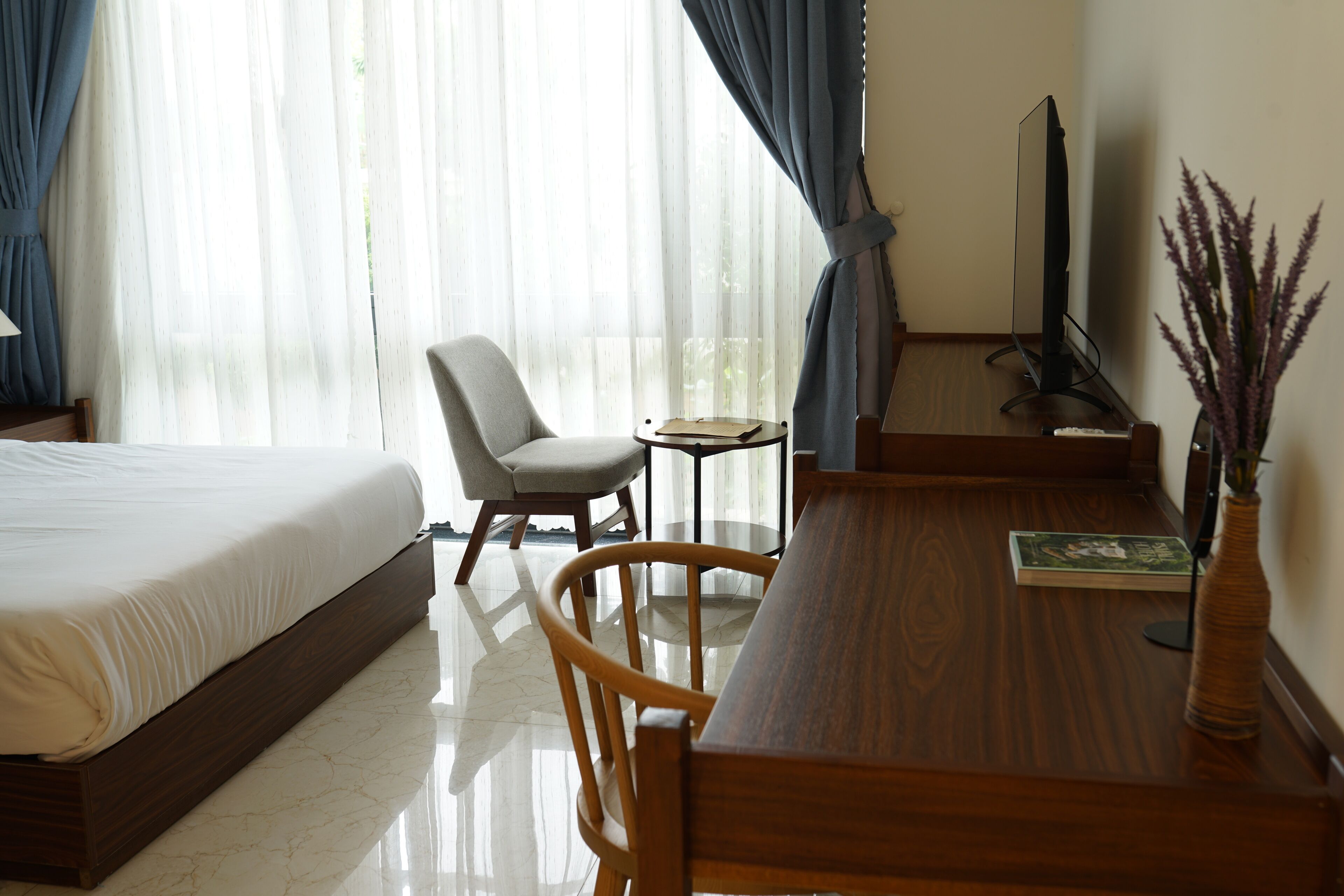 Ein Hotelzimmer mit Bett, Schreibtisch, Stuhl, Fernseher und einem Fenster mit Vorhängen.