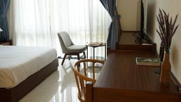 Ein Hotelzimmer mit Bett, Schreibtisch, Stuhl, Fernseher und einem Fenster mit Vorhängen.