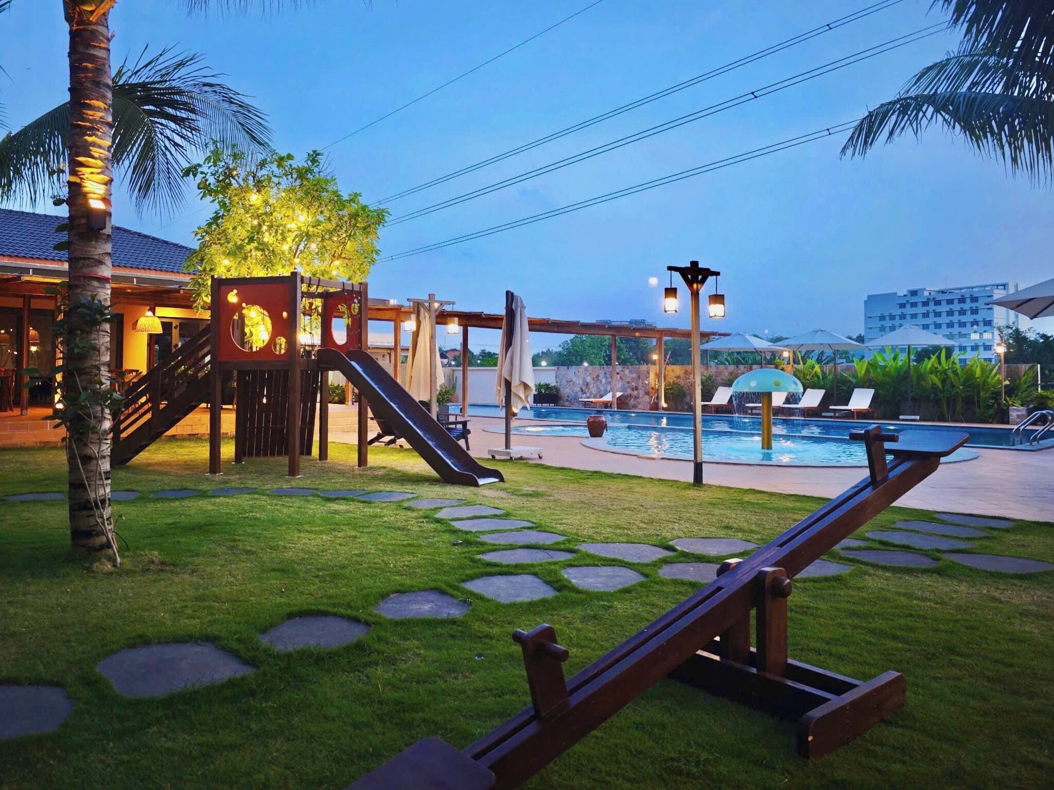 A playground with a slide and climbing structures, a pool area with lounge chairs, and a stone pathway.