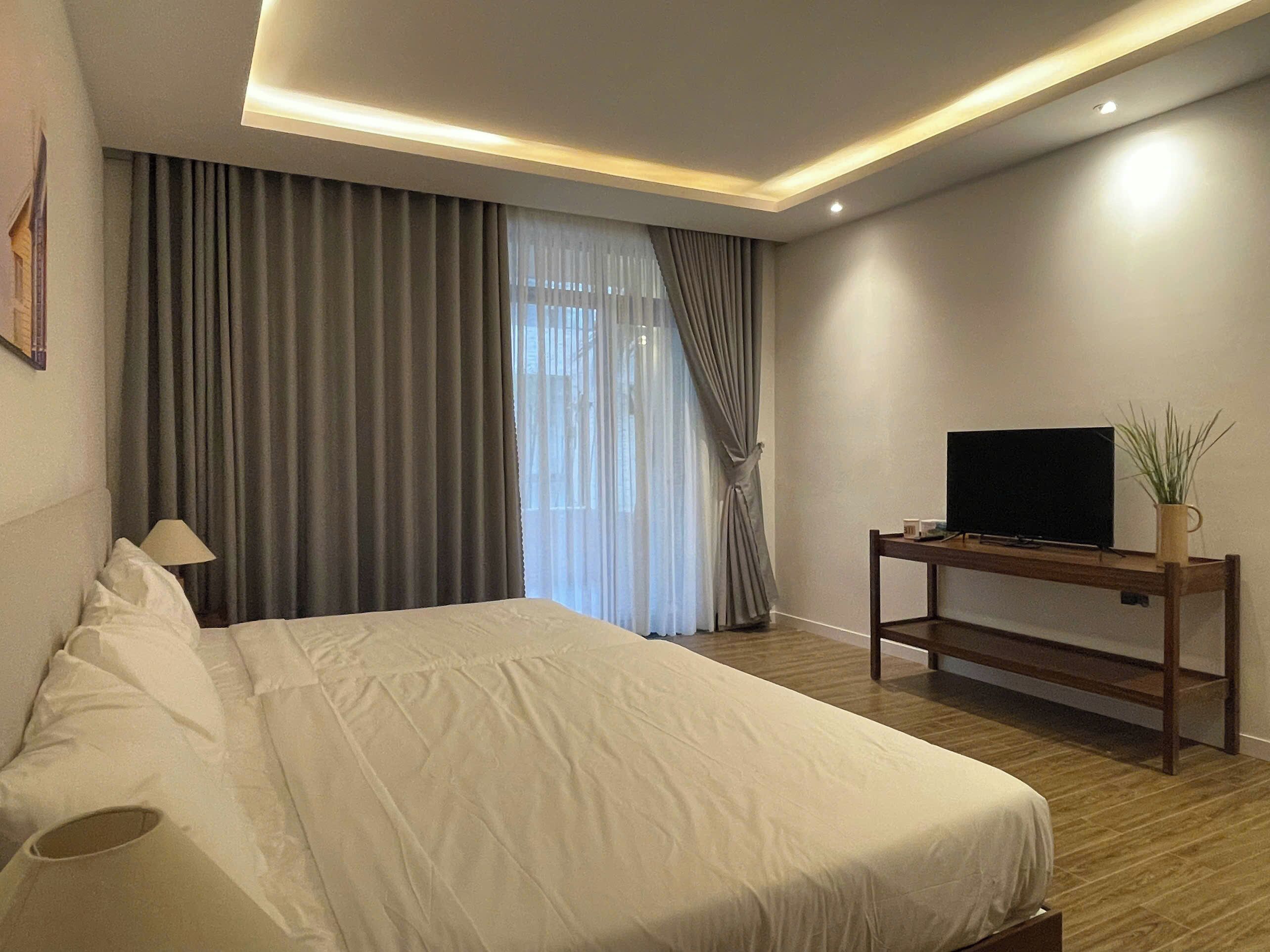 Ein modernes Hotelzimmer mit einem großen Bett, einem Flachbildfernseher auf einem Holzboden und einem Fenster mit Vorhängen.