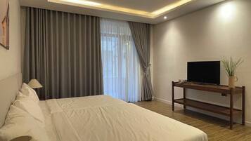 Ein modernes Hotelzimmer mit einem großen Bett, einem Flachbildfernseher auf einem Holzboden und einem Fenster mit Vorhängen.