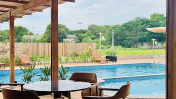 A pool area with a wooden pergola, lounge chairs, and a table with chairs.