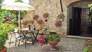 An outdoor patio with a table and chairs, a wine bottle, and potted plants against a stone wall. - Noce Cottage With Pool, Casole D'elsa (Casole D'elsa)