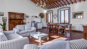 Uma sala de estar acolhedora com sofás listrados, uma mesa de jantar com cadeiras, uma área de cozinha com micro-ondas e uma lareira.
