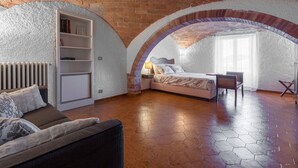 Een slaapkamer met een bakstenen plafond, een bed, een slaapbank, een klein tafeltje en een boekenplank.