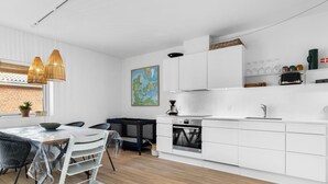 A modern kitchen with white cabinetry, a dining area with a table and chairs, and a large window with a view of a brick wall.