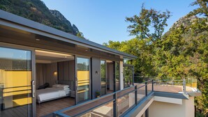 A modern hotel room with a balcony, large sliding glass doors, a bed, and a view of the surrounding nature.