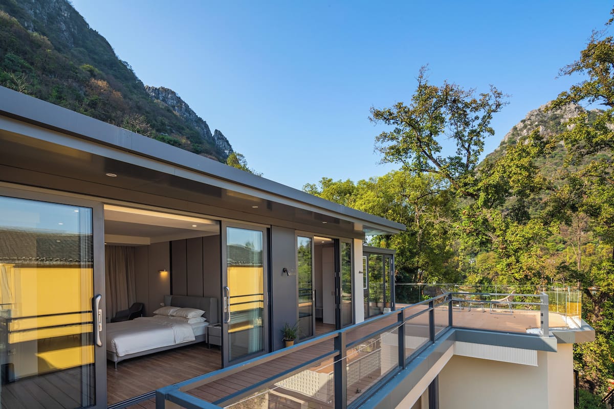 Ein modernes Hotelzimmer mit Balkon, großen Schiebeglasfenstern, einem Bett und Blick ins umliegende Grün.