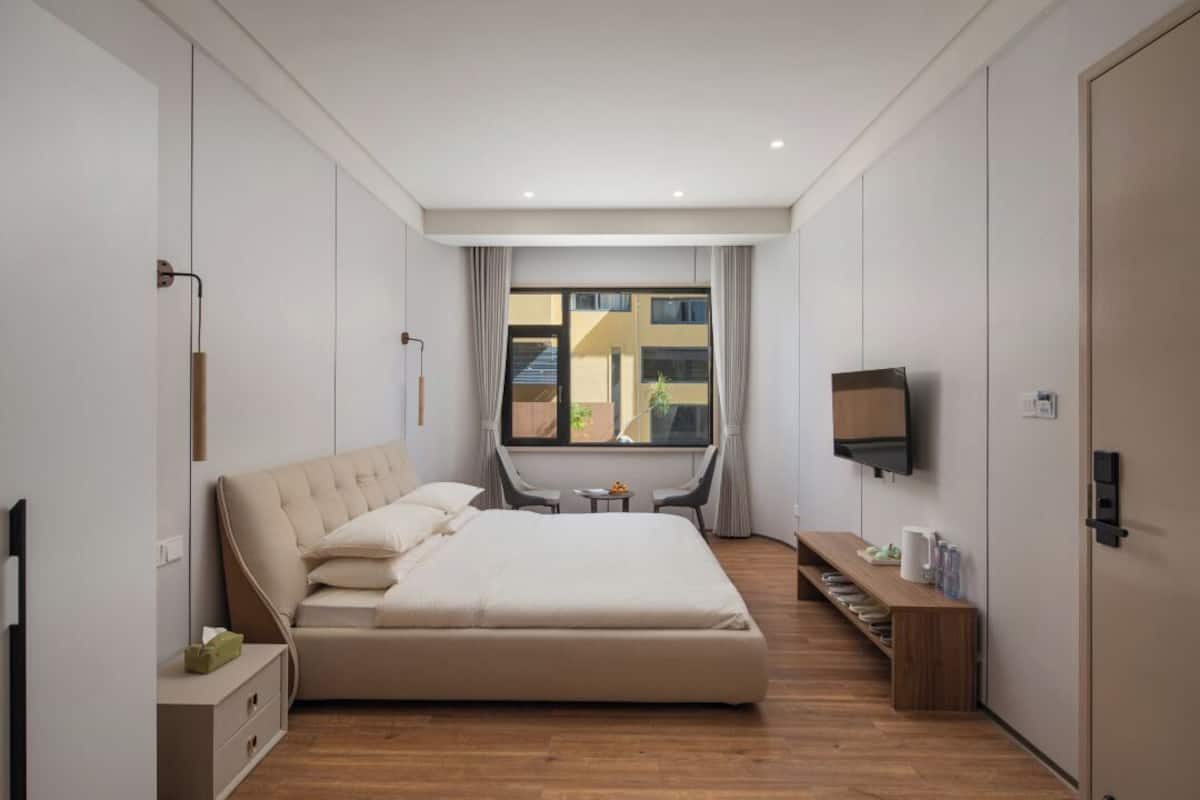 Ein modernes Schlafzimmer mit einem großen Bett, einem an der Wand montierten Fernseher und einem Fenster mit Vorhängen.
