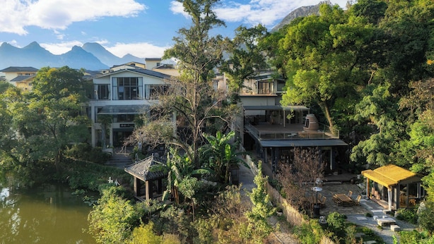 A hillside property with multiple buildings, a pond, and a mountain backdrop.