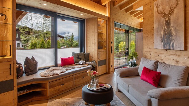 Interior acogedor de una cabaña con un banco de madera, un sofá y un amplio ventanal con vistas a la vegetación.