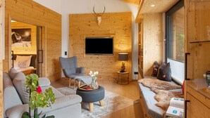 Un salón acogedor con sofá, sillón y televisor instalado en una pared de madera.