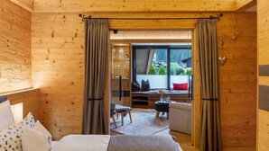 Una habitación con paneles de madera, una cama, una mesita, una silla y un ventanal con cortinas.