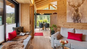Un interior moderno con techo de madera, un sofá con cojines rojos, un comedor y un cuadro grande de un ciervo.