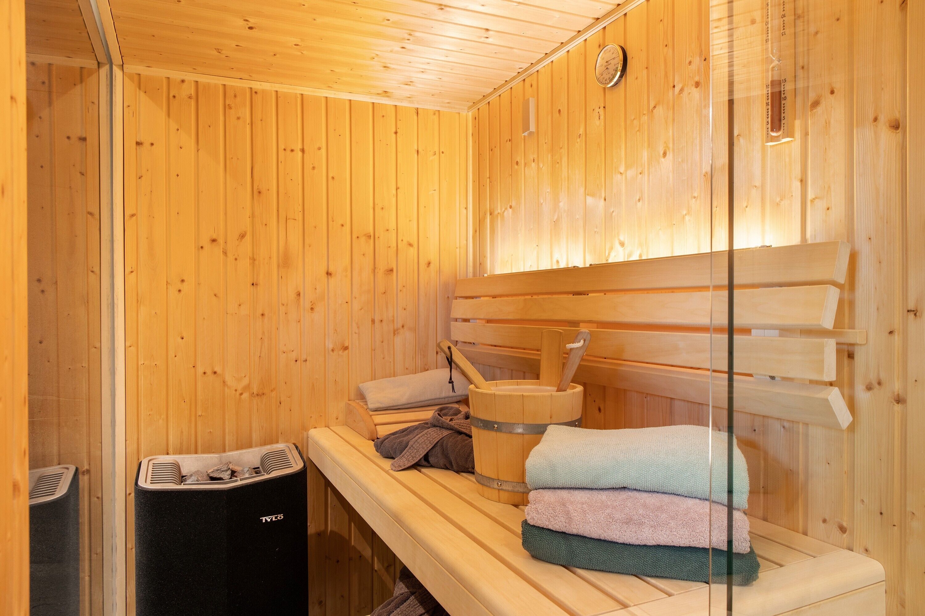 A sauna room with wooden benches, a wooden bucket, and towels.