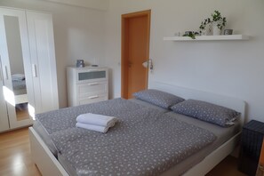 Un dormitorio con cama, armario, mesita de noche y estante con objetos decorativos.