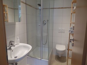 Un baño con ducha envuelta en vidrio, un lavabo blanco y un inodoro.