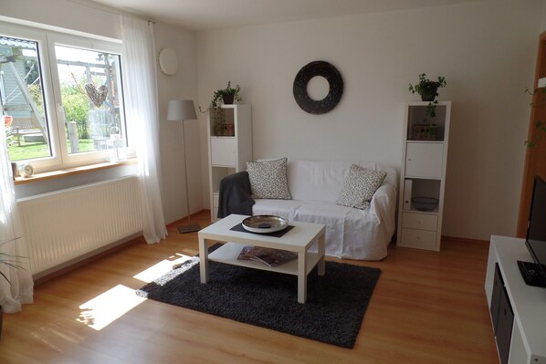 A living room with a white sofa, a coffee table, a black rug, and a bookshelf.