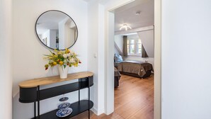 Un couloir avec un miroir rond, un vase blanc orné de fleurs et une console noire sur laquelle est posée une assiette bleue.