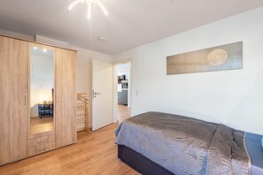 A bedroom with a bed, a wardrobe, and a kitchen in the background.