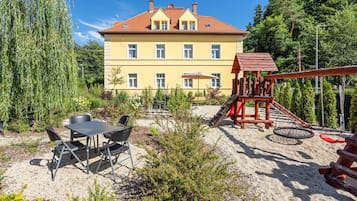 A building with a yellow facade and red roof, surrounded by greenery.