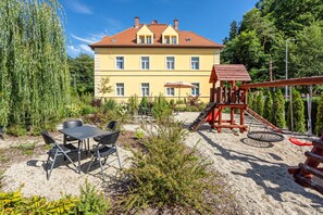 A building with a yellow facade and red roof, surrounded by greenery.