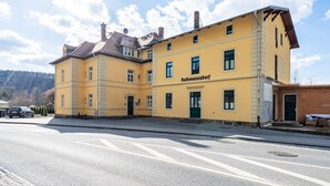 Un bâtiment jaune avec l’inscription « Rathmannsdorf » sur la façade, une rue pavée devant, et un ciel dégagé.