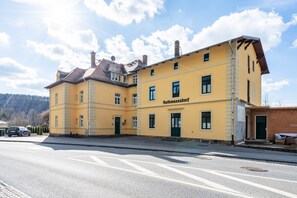 Un edificio amarillo con el nombre 'Rathmannsdorf' en la fachada, una calle pavimentada al frente y un cielo despejado.