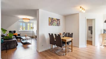 Ein modernes Wohnzimmer mit Essbereich, großen Fenstern und einer Deckenleuchte.