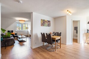 A modern living room with a dining area, large windows, and a ceiling light fixture.