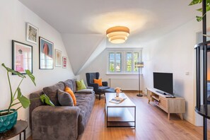 A modern living room with a grey sofa, a coffee table, a TV, and a large window with a view of greenery.