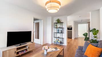 A modern living room with a flat-screen TV, wooden entertainment unit, and a coffee table with a magazine and flowers.