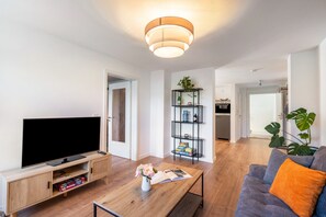 Un soggiorno moderno con televisione a schermo piatto, mobile TV in legno e tavolino da caffè con una rivista e fiori.