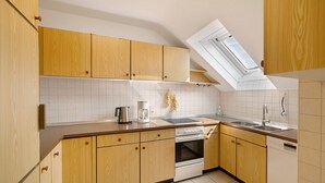 Una cocina con armarios de madera, horno empotrado, lavavajillas y un tragaluz.